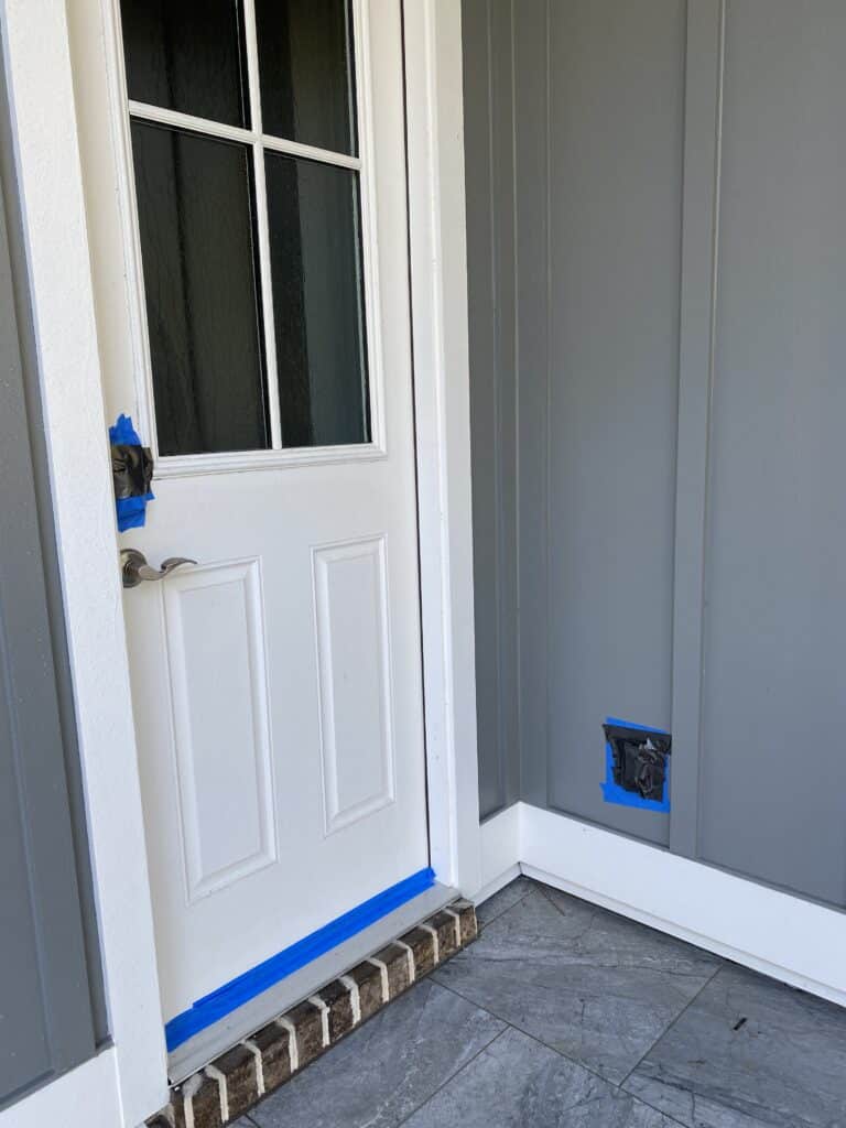 Preparation for a house soft wash, with painter's tape sealing an outdoor electrical outlet, a keyless entry lock, and the bottom of a door to prevent water damage.