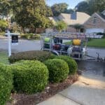 Professional pressure washing trailer parked in front of a realtor's yard sign at a clean home, showcasing our pressure washing services in Tallahassee, FL.