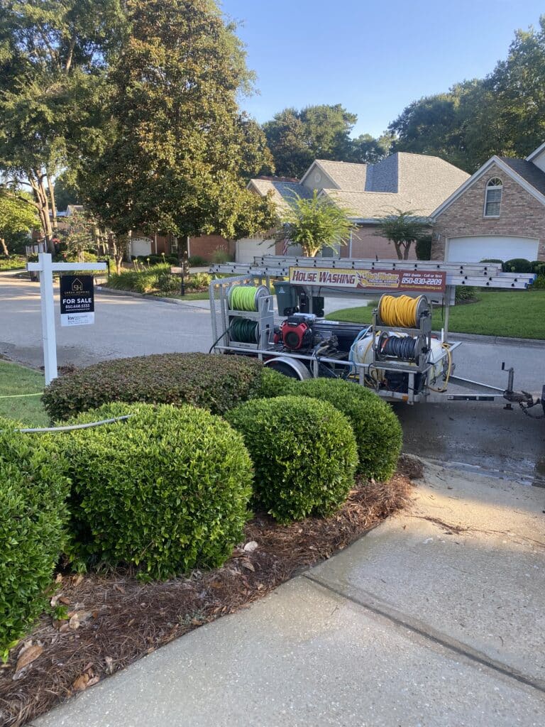 Professional pressure washing trailer parked in front of a realtor's yard sign at a clean home, showcasing our pressure washing services in Tallahassee, FL.