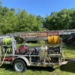 The Hot Water Pressure Washing company trailer, equipped for soft washing, featuring a large sign that reads 'Tallahassee's Best House Washing'.