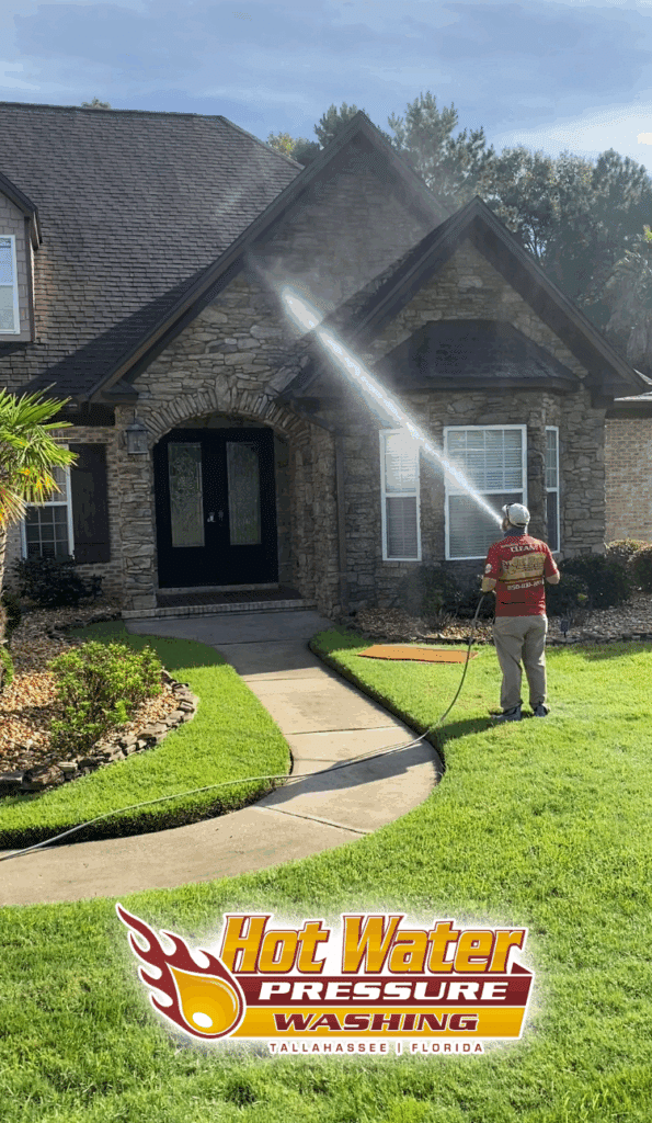 A Hot Water Pressure Washing technician carefully applying a low-pressure soft wash solution to the siding of a home in Tallahassee, Florida.
