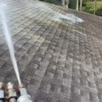 Hot Water Pressure Washing soft wash system spraying the perfect ratio of sodium hypochlorite solution to clean a shingle roof in Tallahassee, Florida.