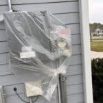 Whole-house generator transfer switch covered in plastic to protect it from water damage before a pressure washing and Soft Wash House Washing project in Crawfordville, Florida, near Tallahassee, Florida.