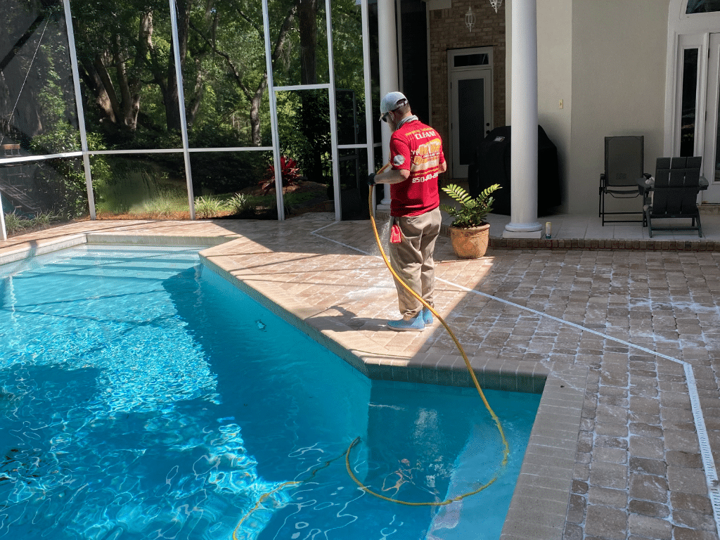 A Hot Water Pressure Washing professional safely soft washing a brick paver pool deck under a screen enclosure in the Baker Place neighborhood of Tallahassee, Florida.