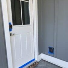 Preparation for a house soft wash, with painter's tape sealing an outdoor electrical outlet, a keyless entry lock, and the bottom of a door to prevent water damage.